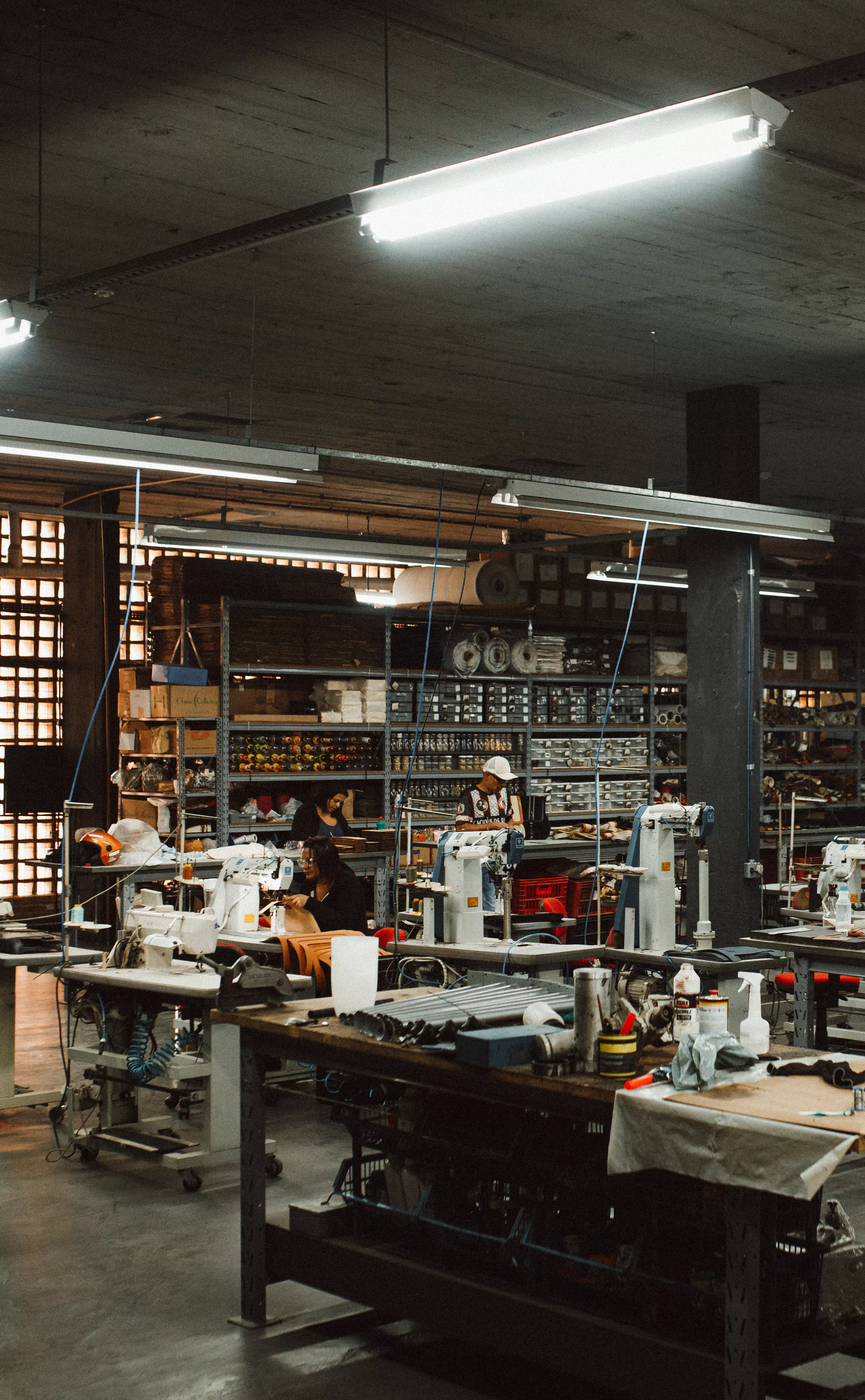 Interior do estúdio DIWO. Lugar amplo com máquinas de costura, mesas de trabalho, tecidos e estoque.