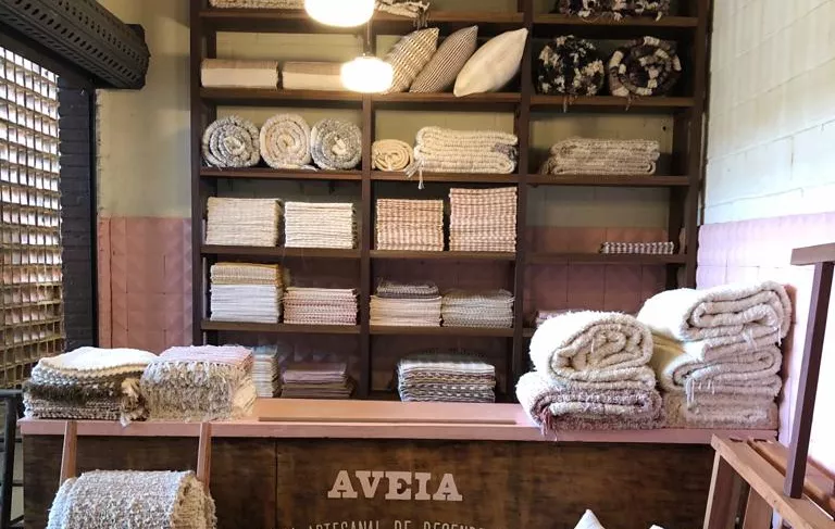 Interior da loja Aveia Tapeçaria. Lugar pequeno com produtos expostos em mostruários e estantes.